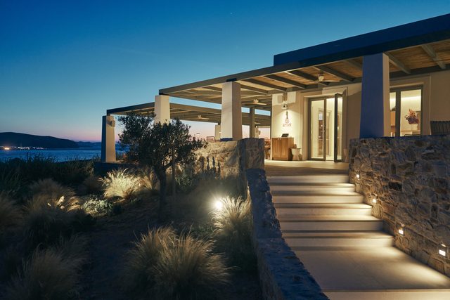 The lit stone path and steps up to the restaurant entrance after dark, the sea and the lights of the village behind