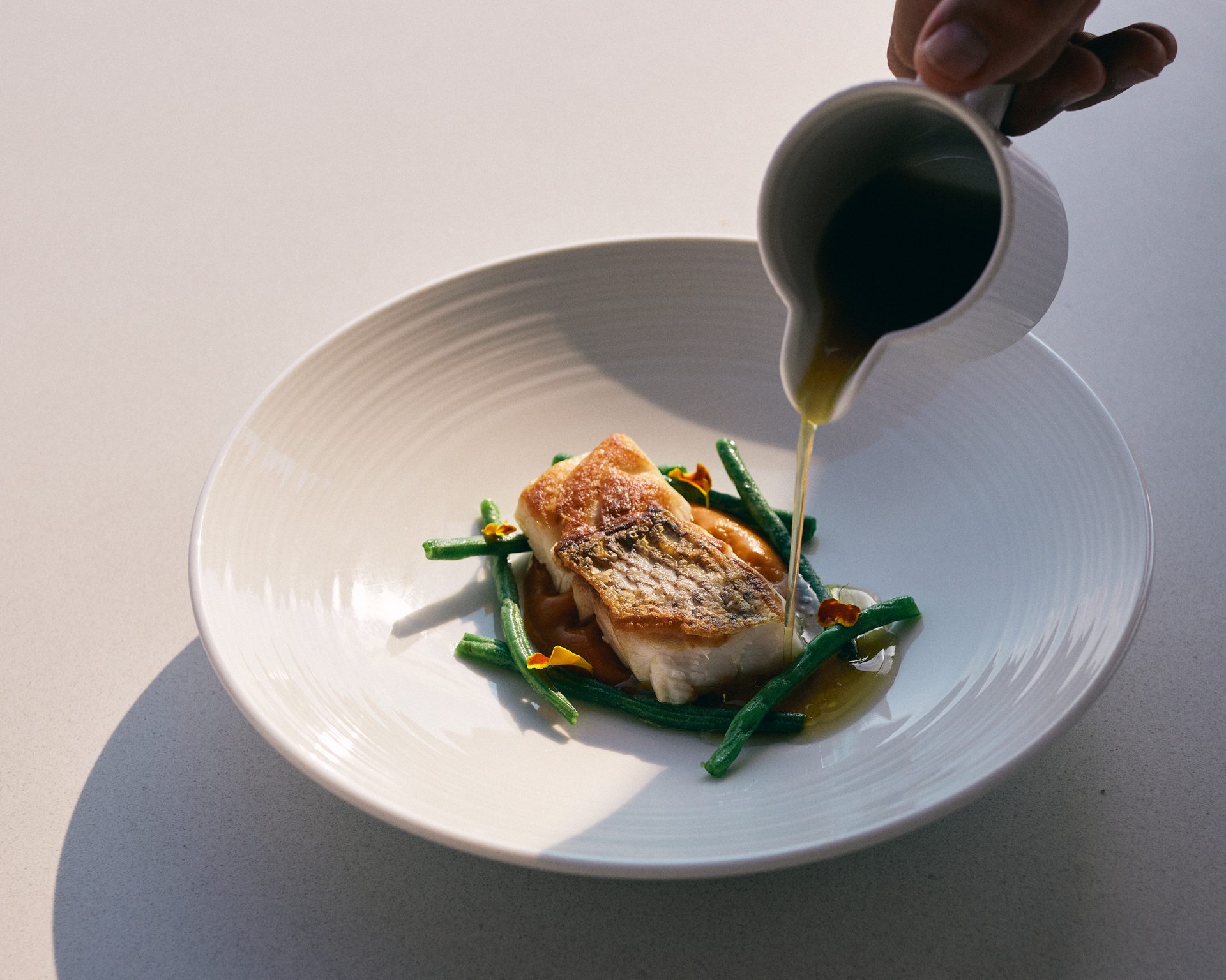 Summer-vegetable broth poured from a jug over the dentex with tomato glaze and green beans