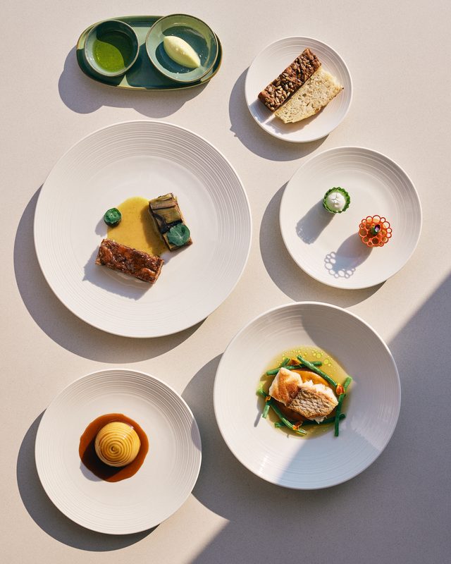 The tasting menu's courses laid out from above on white plates in hard afternoon light