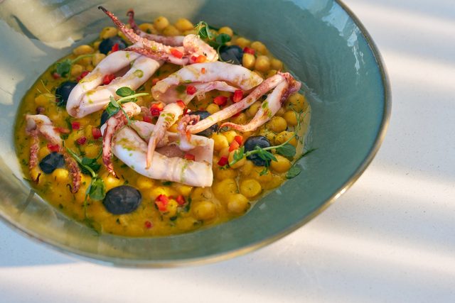 Chickpeas in a saffron-coloured broth with grilled squid, red pepper and herbs, in a green-glazed bowl