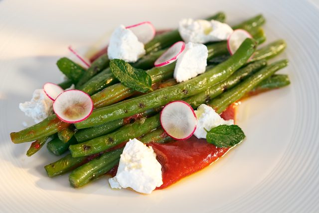 Grilled green beans piled over red pepper cream, with spoonfuls of soft goat cheese, sliced radish and mint leaves