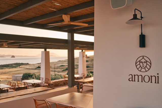 The amoni mark painted on a white plaster wall beside the open terrace, warm evening light on the tables beyond