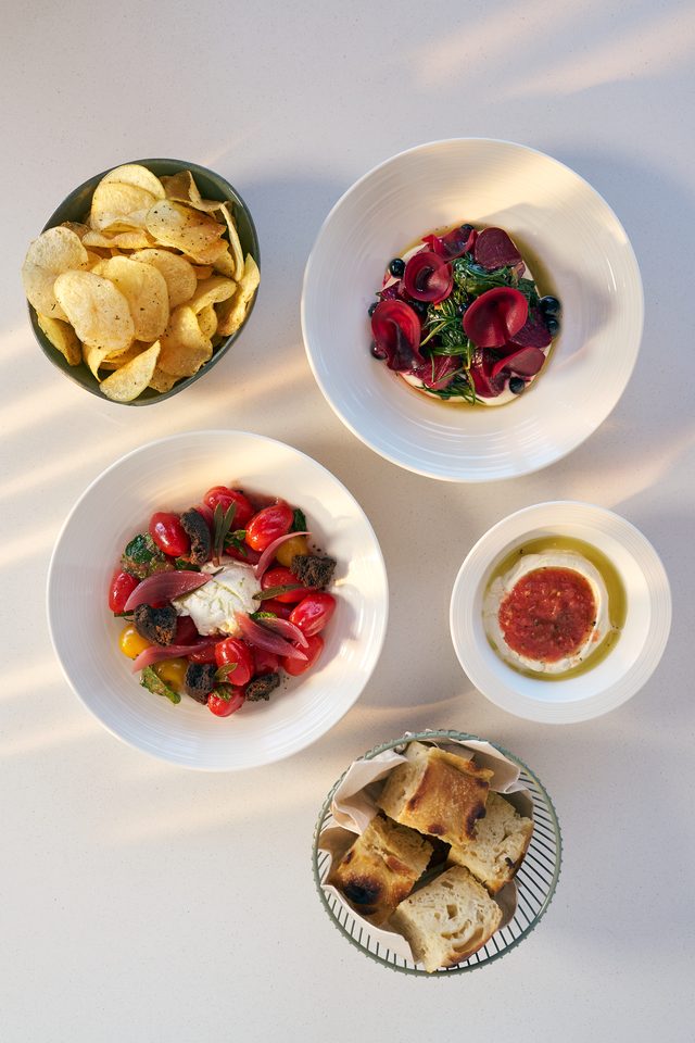 Several small plates seen from above — potato crisps, a beetroot dish, a tomato salad, a bowl of fish roe dip and a basket of bread