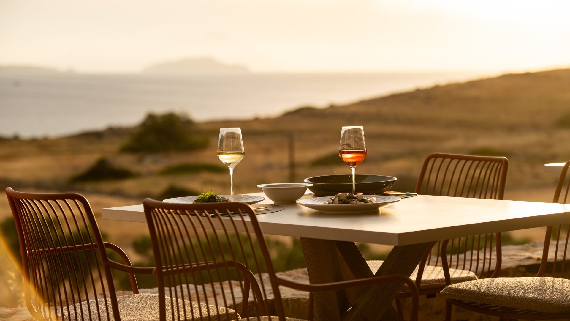 The terrace by day, striped shadow from the reed pergola falling across long wooden tables that look straight out over the Aegean